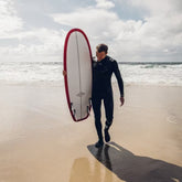 Man in a wetsuit holding a surfboard on a beach with waves in the background